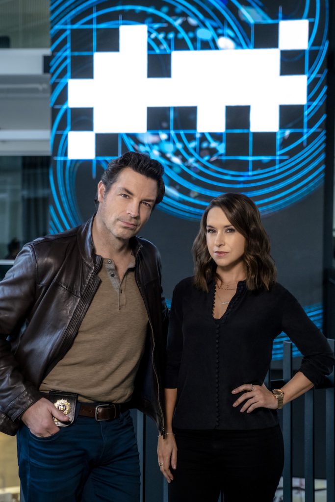 Hallmark, After volunteering to participate in a crossword solving competition with a new supercomputer, crossword puzzle editor Tess Harper finds herself swept into the investigation of the bizarre murder of a tech CEO. Photo: Brennan Elliott, Lacey Chabert Credit: ©2021 Crown Media United States LLC/Photographer: Allister Foster